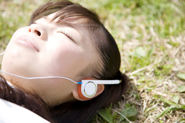 芝生に寝転がりながら音楽を聴く女子高生