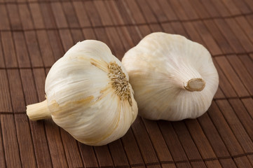 Two garlic heads on a bamboo mat.