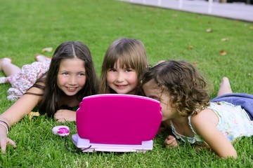 Three little girl playing with toy computer in grass