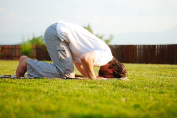 Muslim male is praying outdoor on green ground