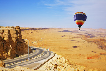 The bright decorative balloon soars above road to desert