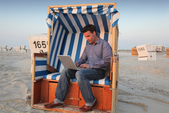 Junger Mann mit Laptop und Computer am Strand