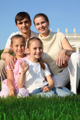 family of four outdoor in summer sits on grass
