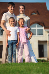 family from four stands on grass against house