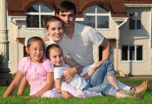 family from four sits on grass against house