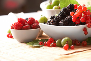 Berries in plates, on a table, among green leaves