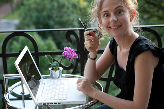 junge blonde Frau schreibt auf einem Laptop Computer auf Balkon