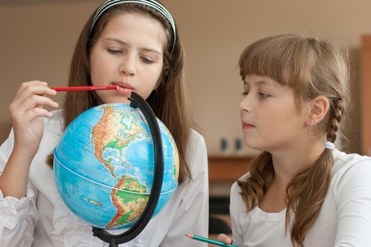 Two schoolgirls search geographical location using globe