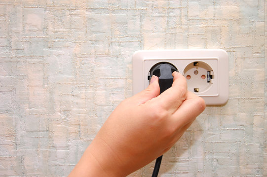 female hand sticks a plug in the socket