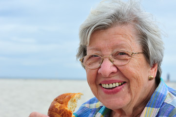 Seniorin isst Croissant am Strand