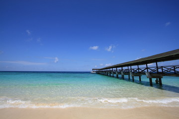 Blue sky with long wooden bridge on the clear water beach