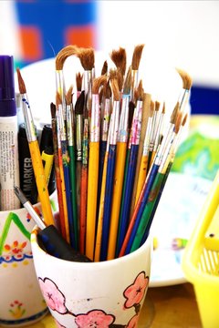 many paintbrushes and markers are standing on artist`s table