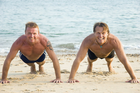 Two happy smiling men exercising on the beach.