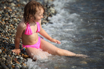 little girl sits ashore in waves