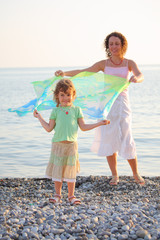 Mother with daughter stand on seacoast with shawl in hands