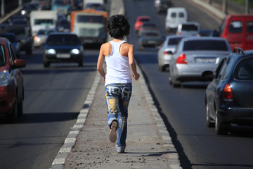 girl runs on highway middle in city, view from back