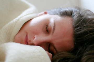 junge Frau schläft auf Couch unter weißer Decke