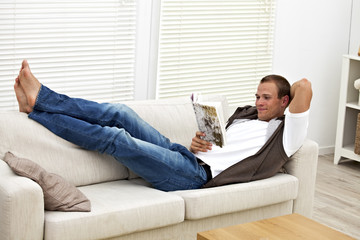 lächelnder jungen Mann auf einer Couch liest ein Buch