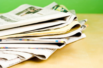 Stack of newspapers lying on the table on green background