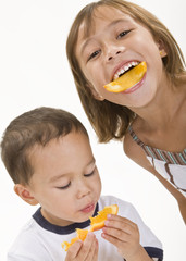 Two young children enjoying orange peel slices