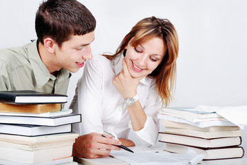 Young female and male models sitting on desk with many books - obrazy, fototapety, plakaty