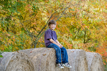Naklejka na ściany i meble Boy Sitting on Hay Bales in the Fall