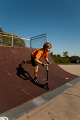 Fototapeta na wymiar Kind mit Scooter, Roller, übt auf der Skatebahn Tricks