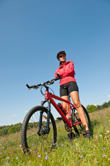 Sportive woman with mountain bike in meadow
