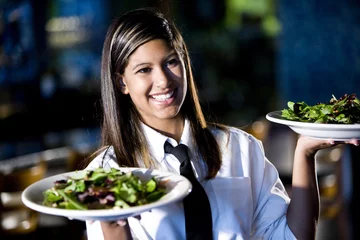 Selbstklebende Fototapete Restaurant Hispanische Kellnerin serviert zwei Salatteller in einem Restaurant