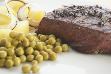 grilled pepper steak with some pea and potato on a white plate