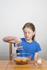young girl pouring oil into mixing bowl while baking a cake