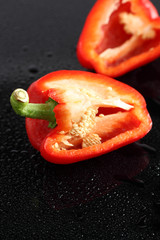 Paprika, rot, halbiert, auf schwarzem  Acryl