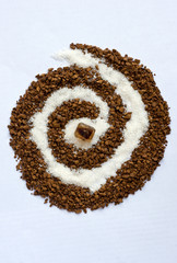 Spiral of coffee and white sugar with a cane sugar cube on white