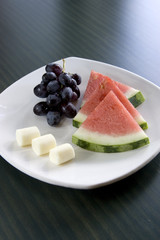 A plate of watermelon, cheese, and grapes.