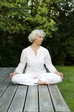 Seniorin meditiert im Grünen auf der Sonnenterrasse