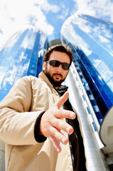 Young attractive man in front of modern building giving a hand