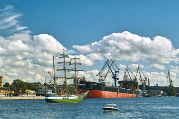 Retro tallship near modern vessel and derricks in the dockyard