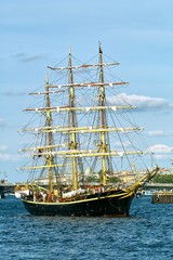 Black sailboat with yellow masts at the background of blue sky