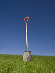 Shovel in green grass against a blue sky