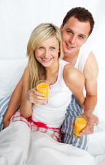 Obraz na płótnie Canvas Couple holding orange juice glasses in bed