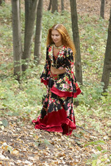Obraz na płótnie Canvas A beautiful ginger-haired girl in gipsy suit in forest