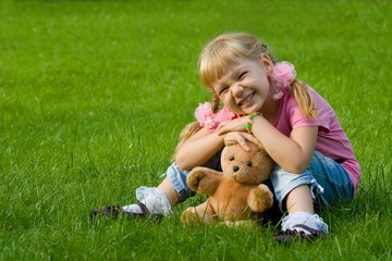 Cute little girl in grass with teddy bear.