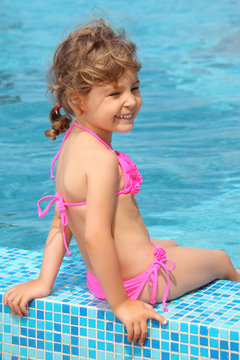 little girl sits on border of pool