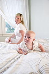 Fototapeta na wymiar Cute baby crawling on bed while mother watches