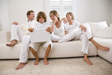 Boy using laptop sitting with family on white sofa