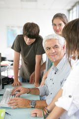 homme souriant près d'adolescents devant un ordinateur fixe