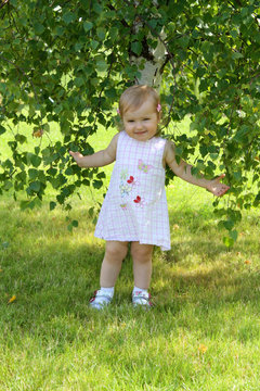 Smiling baby girl standing near the birch