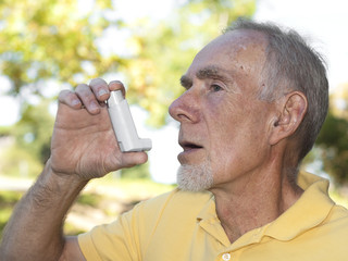 Elderly man using asthma inhaler outdoors
