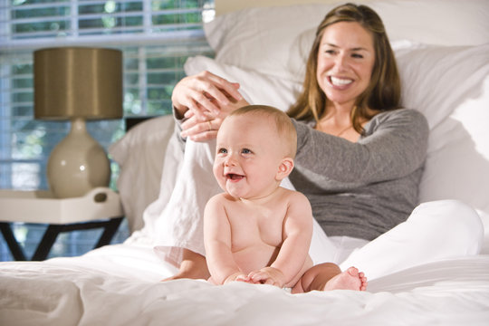 Mother sitting on bed with amused six month old baby