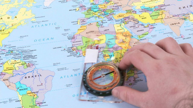 Hand moving a compass over a world map